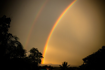 Rainbow in sky evening over residential, trees in Thailand city with dark sunshine in summer