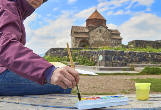 Woman is drawing in ancient monastery Sevanavank in Armenia.