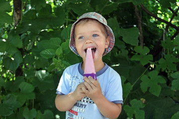 A little boy is happy because there is ice cream. A happy child is eating pink ice cream on the street.