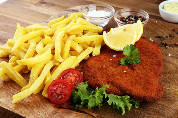 Wiener schnitzel and French fries served with sauces and salad on rustic wooden table