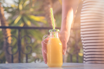 Female holding glass bottle of fresh orange juice on table outdoors