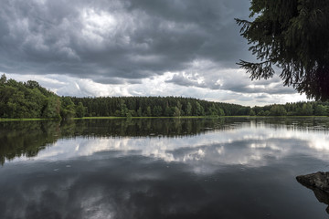 Lake in the middle of a forest with mirroring storm clouds
