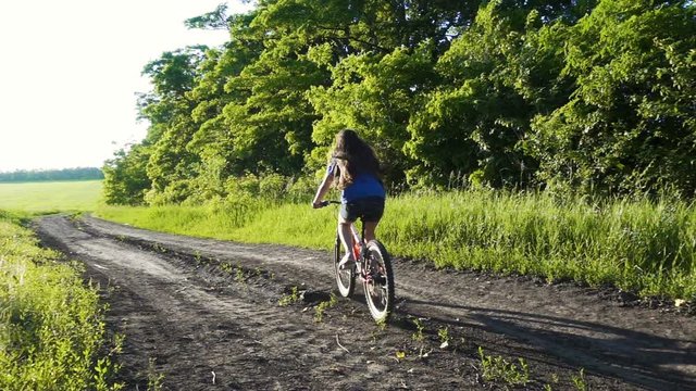 Young girl riding on bike on country road at sunset