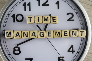 close up shot of a clock with wooden letter blocks forming the phrase time managemnt