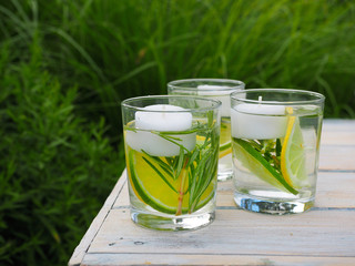 Natural homemade repellent on white wooden table. Sllice of lime and lemon, tea light candles, fresh rosemary and water in three glasses.