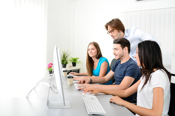 group of young people in a business school office classroom working on desktop computer with teacher
