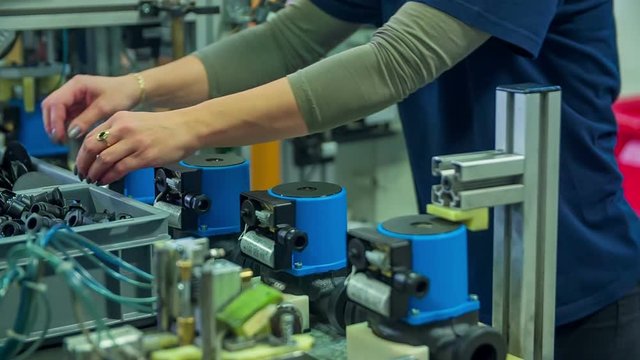 A young woman in the factory is putting the cover on the top of the item. She is working behind a conveyor belt.