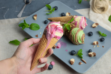 Ice cream cones on grey vintage background. Blueberry, strawberry, mint and chocolate Ice cream in the hand