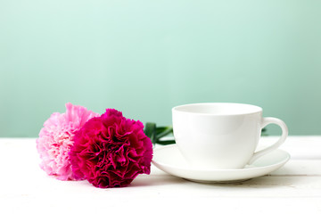 Carnation flower and cup on white wooden table mint background. Retro effect style.