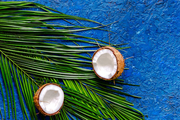 Fototapeta na wymiar Appetizing coconut and palm branch on blue table background top view copyspace