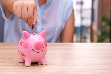 Obraz na płótnie Canvas woman hand putting a coin into a pink piggy bank on wooden desk - save money concept.
