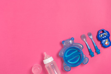 Baby bottle and blue plate with spoon and fork isolated on pink. Top view