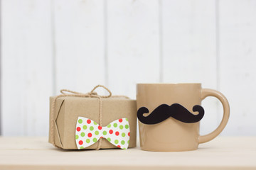Gift box, coffee cup, paper mustache, tie on wooden background with copy space. Greetings and presents. Happy Father's Day.