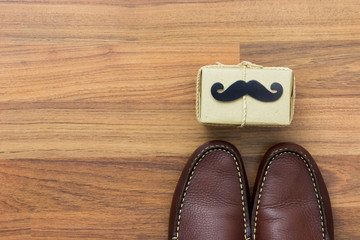 Fototapeta na wymiar Gift box, paper mustache, shoes on wooden background with copy space. Greetings and presents. Happy Father's Day.