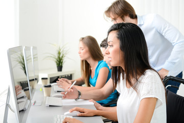 group of young people in a business school office classroom working on desktop computer with teacher