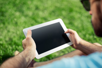 Young man using and typing tablet computer in summer grass.