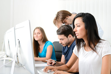 group of young people in a business school office classroom working on desktop computer with teacher