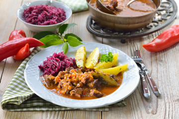 Deftige Hausmannskost: Pikantes ungarisches Gulasch mit Petersilienkartoffeln und Rotkraut serviert – Hot Hungarian goulash served with parsley potatoes and red cabbage