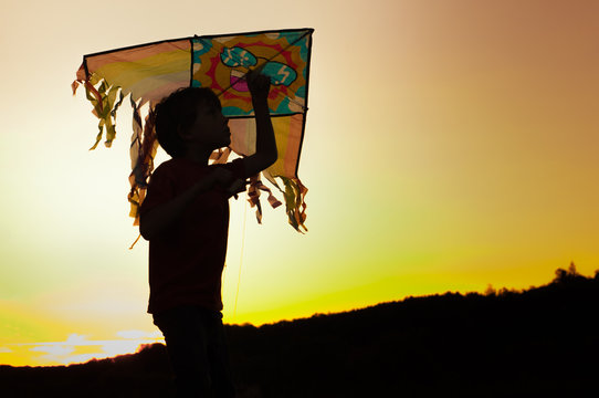 A boy is launching a kite at sunset