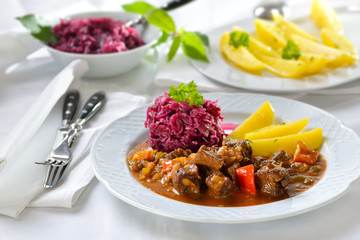 Deftige Hausmannskost: Pikantes ungarisches Gulasch mit Petersilienkartoffeln und Rotkraut serviert – Hot Hungarian goulash served with parsley potatoes and red cabbage