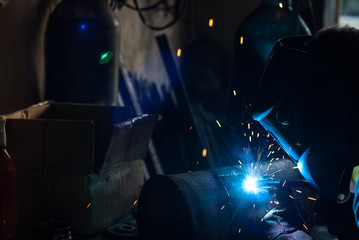 The silhouette of a welder, a tank of oxygen,
