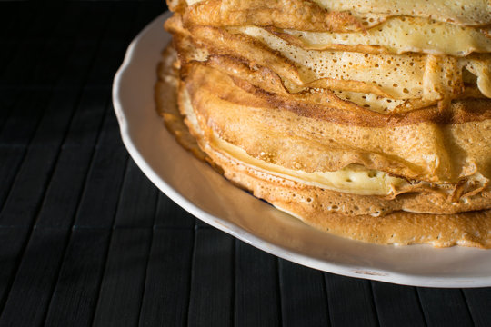 Stack of English pancakes on a round white plate on a black background. Shrove Tuesday, Pancake Day in Britain. Appetizing russian pancakes for Maslenitsa carnival (Shrovetide)
