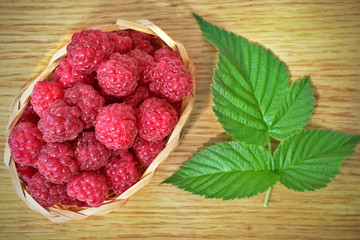 Raspberry basket on wooden background with leafs