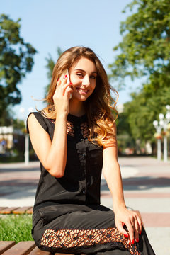 Portrait of a young smiling beautiful woman talking on the phone in park