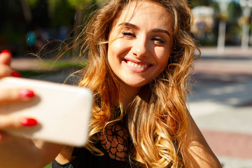 Portrait of a beautiful young woman making selfie on smart phone in the park. Happy young woman photographing herself.