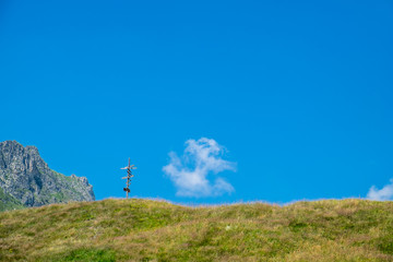 Fototapeta premium Mountain peaks, sky, clouds, meadows and a crossroad sign in Grana Valley, Cuneo, Piedmont, Italy.