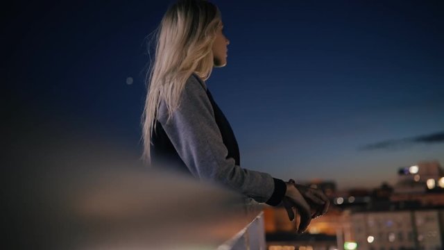 Woman standing on terrace in city at night and looks to cityscape