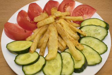 Fried French fries on a white plate with tomatoes and cucumbers.