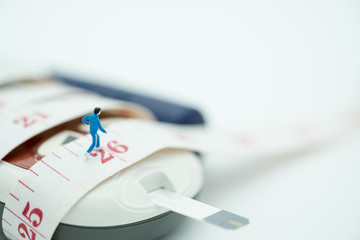 Close up of runner miniature figure running on measure tape binding on Glucose meter with blood sugar test strip and lancet - use for Medicine, diabetes, glycemia, sport, health care andconcept.