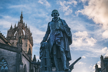 The monument of Adam Smith on The Royal Mile and the apse of the St Giles Cathedral lit by the setting sun at the background. Edinburgh, Scotland, UK - obrazy, fototapety, plakaty