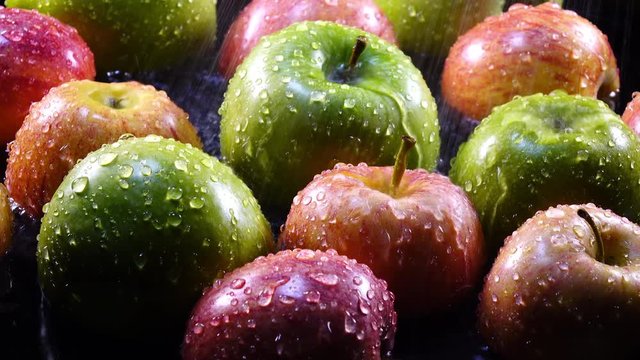 Amazing water flowing and splashing red, pink and green apples in back light close up. Flat lay of yummy fresh fruit with amazing texture in 4k, 3840x2160, clip. Vibrant eco product for healthy food.