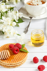 Tea Cup with Jasmine flowers and thin waffles with honey and raspberry on a light wooden background