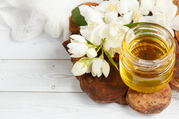 Jar and a spoon with honey on a wooden stand with Jasmine flowers