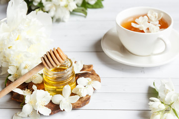 Cup of tea, pouring honey from a spoon in a jar, Jasmine flowers on a light wooden background