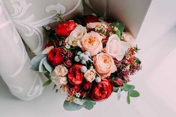Beautiful wedding bouquet of red flowers, pink flowers and greenery stand next to the window