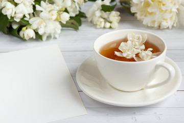 Cup of tea, pouring honey from a spoon in a jar, Jasmine flowers on a light wooden background. Copy space.