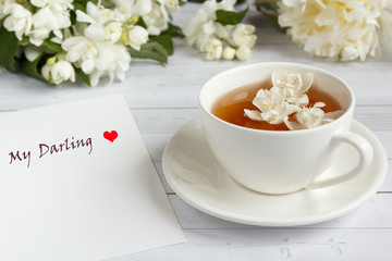 Cup of tea, pouring honey from a spoon in a jar, Jasmine flowers on a light wooden background. Copy space.