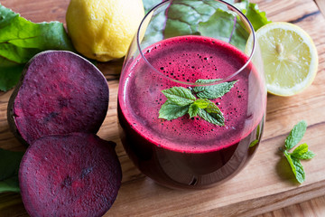 Red beet juice in a glass with lemon and beet greens