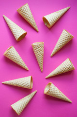 Sugar waffle cone for ice cream arranged in pattern on pink background.  The image with copy space can be used as a background for the design of the confectionery menu, cards, greetings, invitations