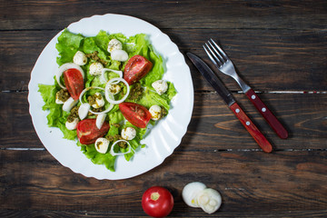 Caprese salad. Cherry-tomatoes, baby spinach and mozzarella in metal bowl with pesto dressing on rustic wooden backdrop, top view