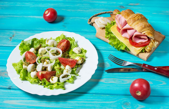 Light and hearty spring breakfast. Croissant with ham, cheese, fresh tomatoes and salad with Mozzarella on a wood table.