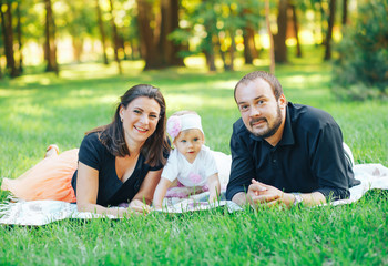 Happy family lies in a park on green grass. Mom dad and little daughter on the meadow