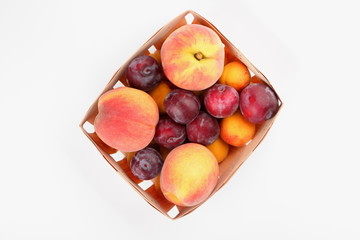 Peaches, apricots and plums in a basket isolated on white background