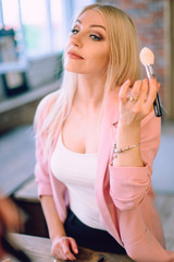 Portrait of a beautiful blonde woman applying makeup near a mirror