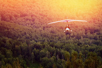 Fototapeta premium paraglider with a motor on the background of mountains and forests, in the setting sun, moves to the camera. The concept of extreme rest in the air.