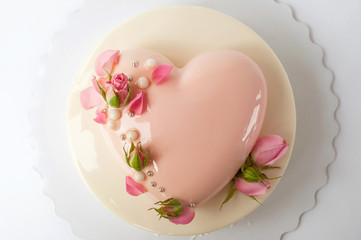 Two-tiered modern french mousse cake with pink mirror glaze in the shape of a heart decorated with roses on a white background. Picture for a menu or a confectionery catalog. Top view. Text space.